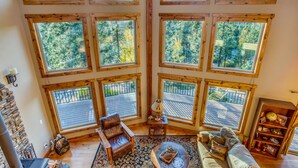A cozy cabin interior with a large skylight, a fireplace, a comfortable seating area, and a rustic wooden bookshelf.