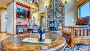 A spacious living area with a stone fireplace, a round wooden table with a bottle of wine, and a leather sofa.