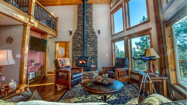 A spacious living room with a stone fireplace, wooden furniture, and large windows offering a view of the outdoors.