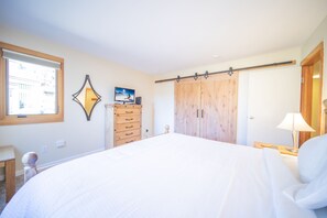 A bedroom with a large bed, wooden wardrobe, and a desk with a lamp. - Quicksilver 1616 (Keystone)