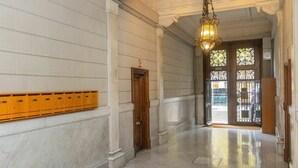 Een gang met marmeren wanden, houten kleedjes en een grote houten deur.