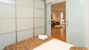 Een slaapkamer met een bed, een beddengoed met een patroon, een nachtkastje en een kledingkast met schuifdeuren.