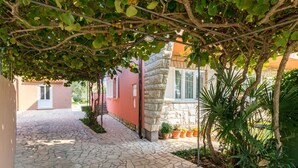 A stone-paved courtyard with a pergola, potted plants, and a red building with a window. - Cosy apartment for 4 people with pool, A/C, WIFI, TV and terrace (Pula)