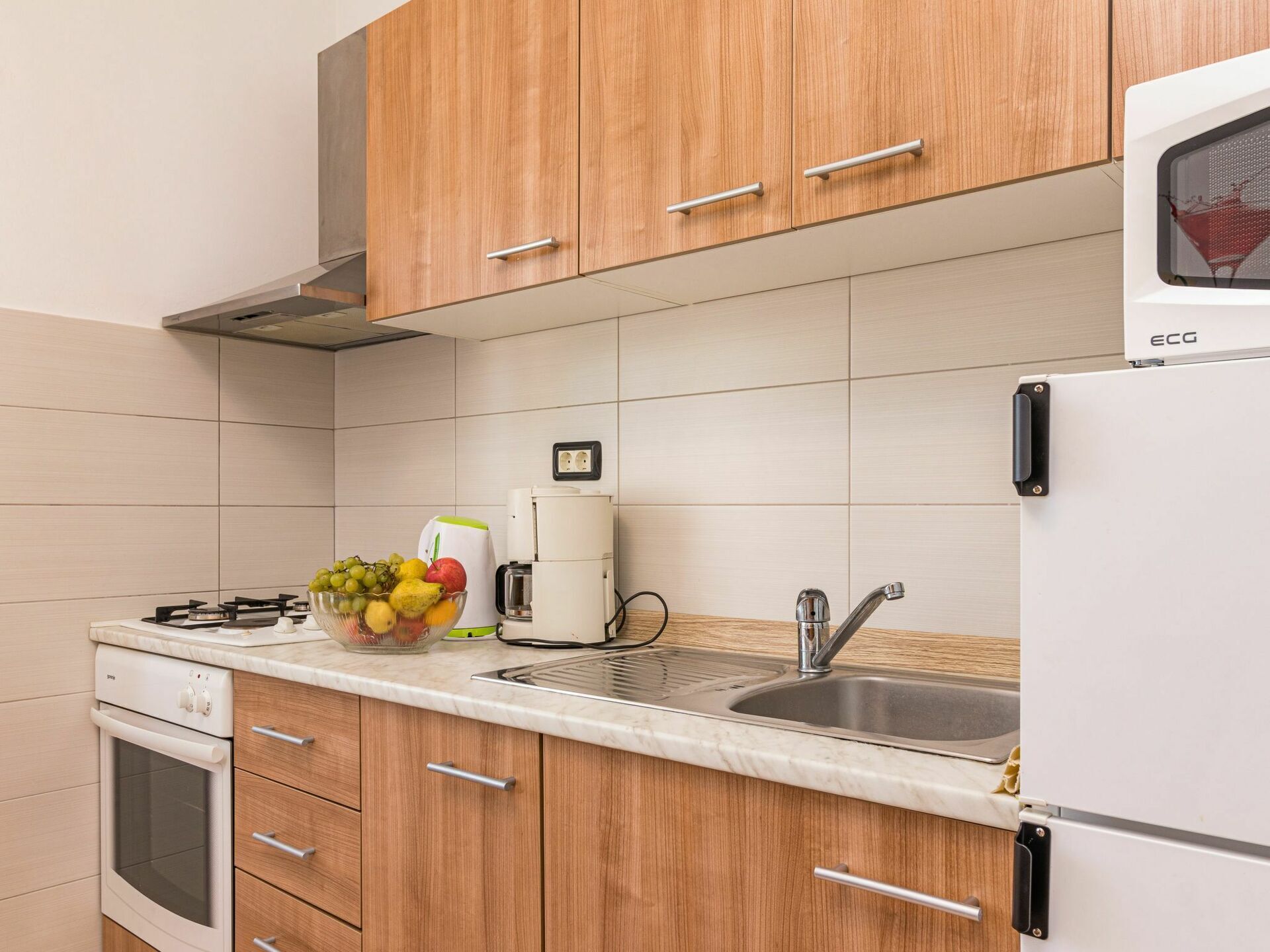 Eine moderne Küche mit Holzschränken, einer Edelstahlspüle, einem Einbauofen und einer Kaffeemaschine.