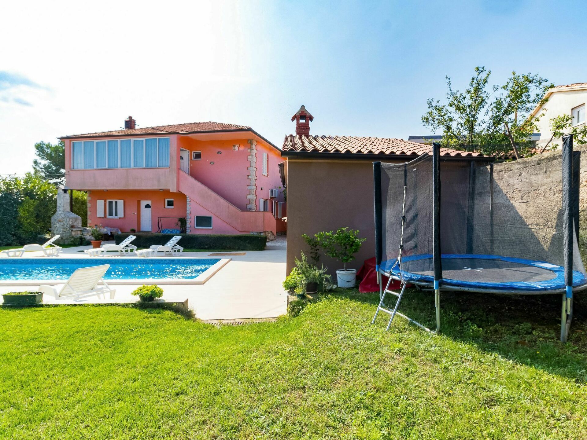 A two-story house with a swimming pool, a trampoline, and a small garden area.
