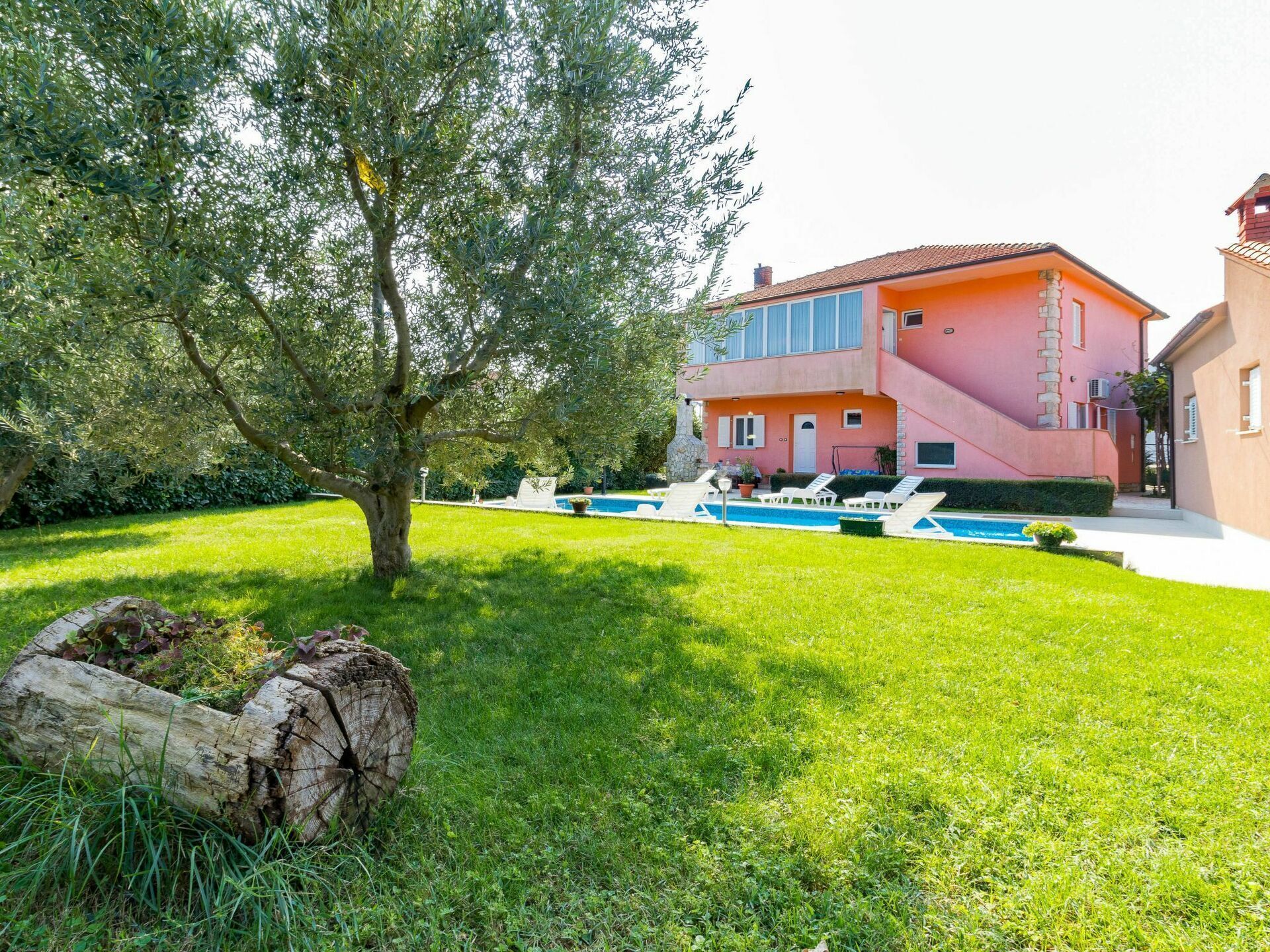 A two-story house with a swimming pool, surrounded by a well-maintained lawn and a large tree.