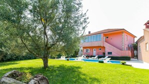 A two-story house with a swimming pool, surrounded by a well-maintained lawn and a large tree.