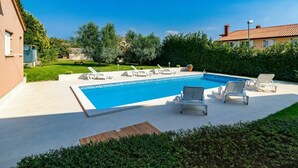 A rectangular swimming pool with a tiled deck, surrounded by lounge chairs and a well-maintained lawn.