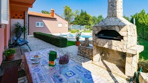 An outdoor patio with a stone-built pizza oven, a pool, and a table set for dining.