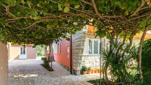 A stone-paved courtyard with a covered walkway, potted plants, and a stone building.