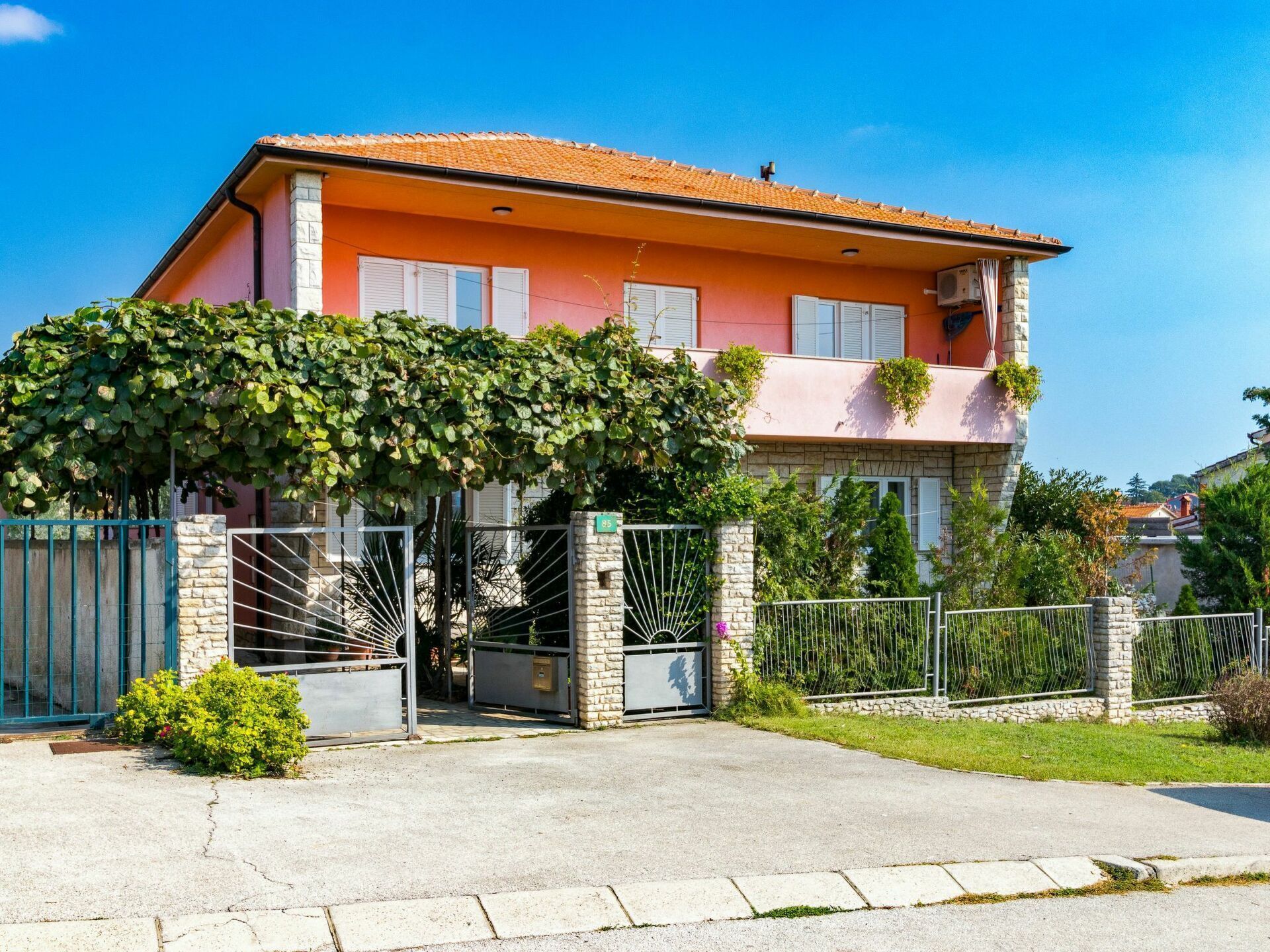 Une maison à deux étages, avec un toit en tuiles, une façade en pierre et une entrée fermée par un portail.