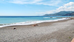 Une plage de galets, un ciel dégagé et des montagnes lointaines.
