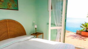 Une chambre à coucher avec un lit, une table de chevet avec une lampe, une fenêtre avec des rideaux et une vue sur la mer.