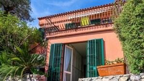 Un bâtiment à deux étages, doté d’une façade en pierre, de volets verts et d’un balcon orné d’une balustrade en fer forgé.