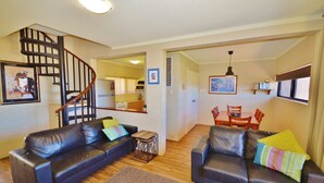 Uma sala de estar com dois sofás de couro, uma mesa de centro de madeira e uma escada que dá para uma cozinha.