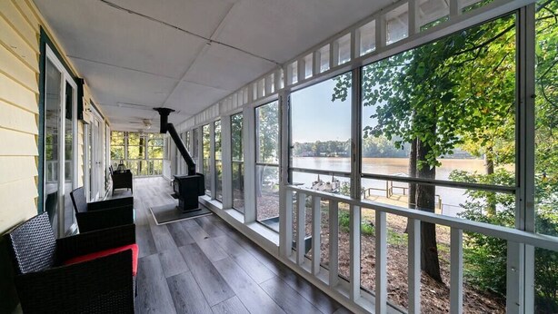 A covered porch with large windows overlooking a body of water, furnished with wicker chairs and a fireplace. - LAY Back in the Lake House (Lilburn)