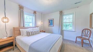 A bedroom with a large bed, two bedside tables, a chair, and two windows.