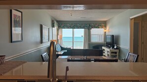 A dining area with a view of the ocean, a television, and a small table with chairs. - Captain's Walk I B1 - Oceanfront in Garden City Beach, SC (Garden City)