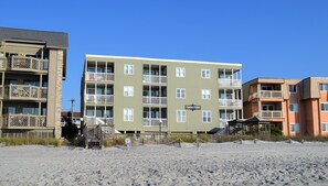 Ein mehrgeschossiges Gebäude mit Balkonen, ein Strand im Vordergrund und ein Schild mit der Aufschrift 'Captain's Walk'.