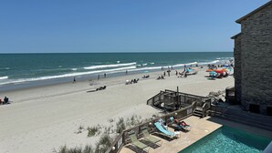 A beach view with a pool area, a wooden deck, and a building with a stone facade. - Captain's Walk I B1 - Oceanfront in Garden City Beach, SC (Garden City)