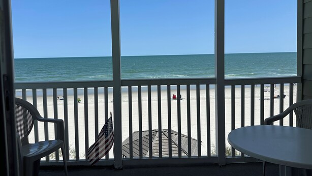A beach view from a covered balcony with white railings, a small table, and two chairs. - Captain's Walk I B1 - Oceanfront in Garden City Beach, SC (Garden City)