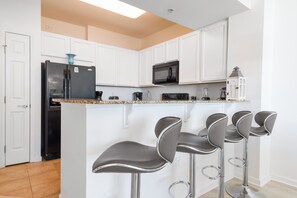 A modern kitchen with white cabinets, a black refrigerator, a microwave, a coffee maker, and three bar stools.