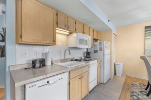 A compact kitchen with wooden cabinets, a microwave, a refrigerator, a sink, and a dishwasher.