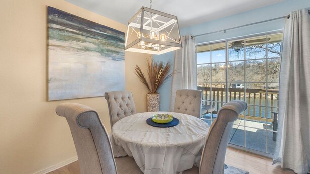 A dining area with a round table, four chairs, a pendant light, a vase with dried plants, and a large painting on the wall. - UP TO 50% OFF Lakeside Branson Condo, Incredible view, Pool, Marina (Branson)