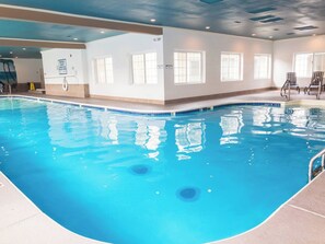 An indoor swimming pool with clear water, a tiled edge, and a poolside area with chairs.