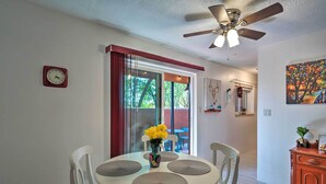 A dining area with a round table, white chairs, a ceiling fan, and a window with red curtains. - Santa Fe Bungalow ~ 2 Mi to Downtown! (Santa Fe)
