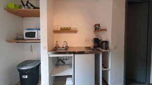 Cuina compacta amb microones, rentamiques i cafetera. Hi ha prestatges sobre la barra que contenen tasses i un cubell de recollida al costat esquerre.