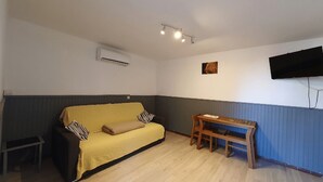Habitació petita i acollidora amb un sofà, una banca de fusta, un aparell d'aire acondicionador i un televisió penjada.