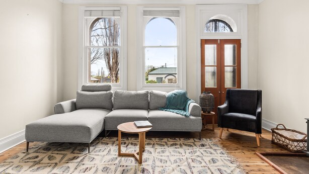 Ein Wohnzimmer mit einem grauen Ecksofa, einem schwarzen Sessel, einem kleinen Holztisch und einem gemusterten Teppich.