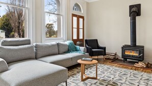 Ein Wohnzimmer mit einem Ecksofa, einem Holztisch, einem Kamin und großen Fenstern.