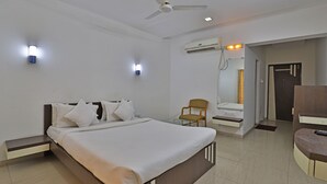 A modern hotel room with a bed, bedside table, chair, and a TV stand. - Utkarsh Hotel (Silvassa)