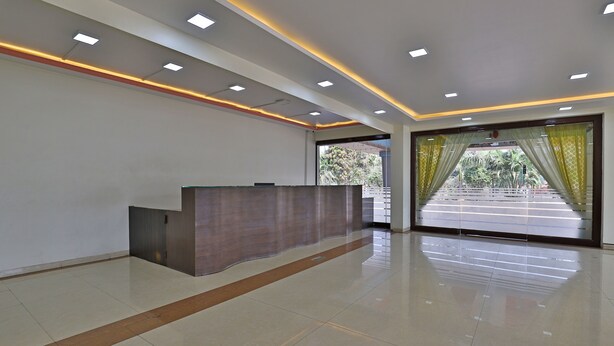 A modern reception area with a reception desk, recessed lighting, and large windows with curtains. - Utkarsh Hotel (Silvassa)