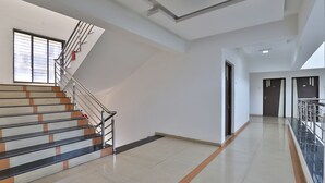 A spacious hallway with a staircase leading to upper floors, featuring a modern design with a glass railing and a tiled floor. - Utkarsh Hotel (Silvassa)