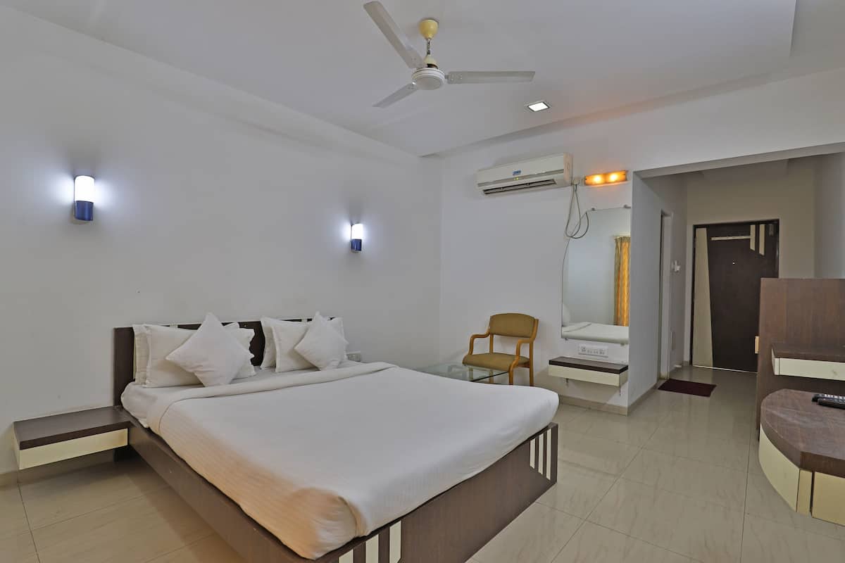 A hotel room with a bed, a chair, a desk, an air conditioning unit, and a ceiling fan.