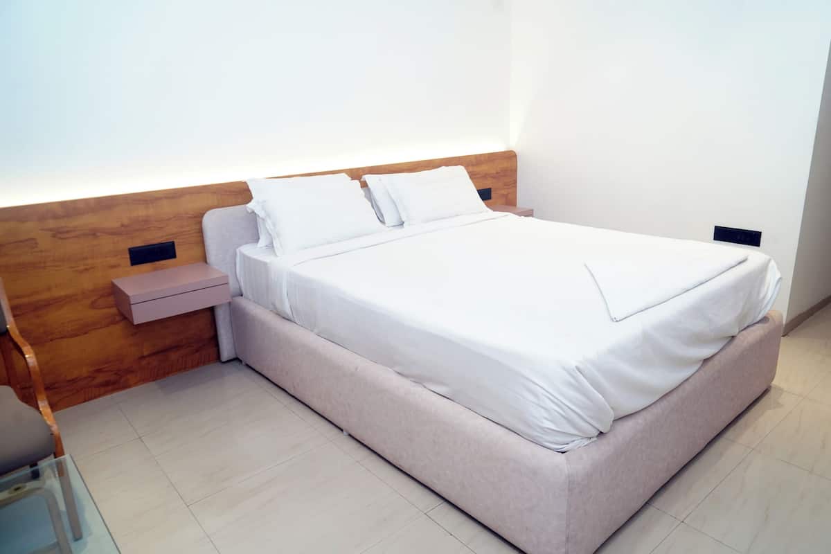 A neatly made bed with white linens, a wooden headboard, and a bedside table with a pink storage box.