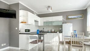 A modern kitchen with white cabinets, a microwave, and a sink. There is a dining area with a table and chairs. - Large Terrance (Kolobrzeg)