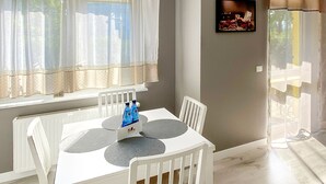 A dining area with a white table and chairs, a radiator, and a window with curtains. - Large Terrance (Kolobrzeg)