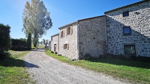 A stone building with a gravel driveway and a large tree.
