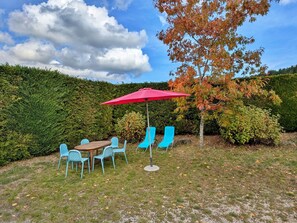 An outdoor seating area with a table and chairs, a red umbrella, and a tree with autumn leaves.