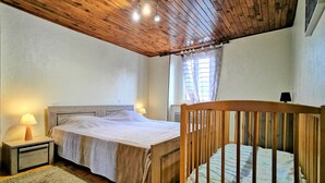 Une chambre avec un plafond en bois, un lit avec une tête de lit en bois, une table de chevet avec une lampe et une fenêtre avec des rideaux.