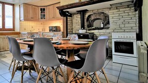 Un coin repas avec une table en bois, quatre chaises, une cuisine avec un mur en pierre, un four à micro-ondes, une cuisinière et une fenêtre.