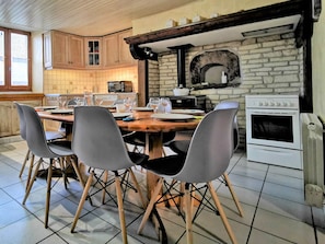 A dining area with a wooden table, four chairs, a kitchen with a stone wall, a microwave, a stove, and a window.