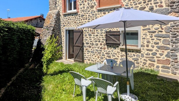 Un bâtiment en pierre doté d’un petit patio, d’un espace extérieur aménagé pour s’asseoir et d’une fenêtre avec des volets.