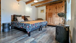 Een rustieke slaapkamer met een houten bed, een grote houten garderobe en een vintage metalen emmer.