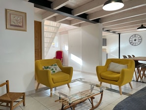 A modern living room with yellow armchairs, a glass coffee table, and a dining area with a clock.