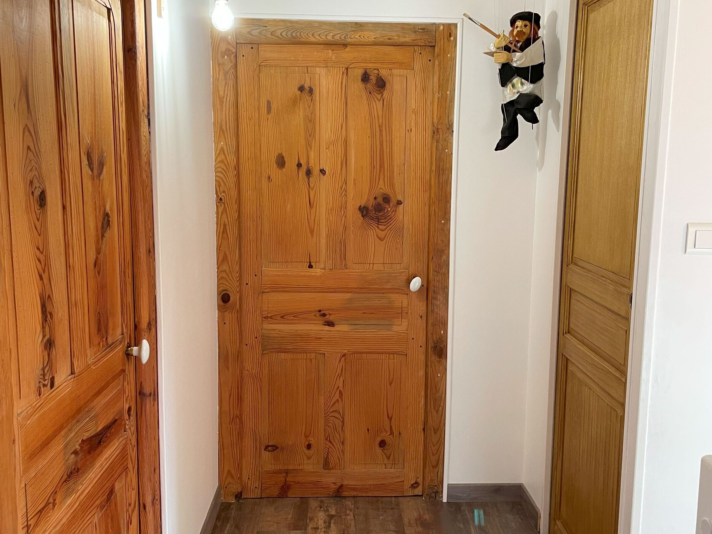 A wooden door with a white handle, a small figure hanging on the wall, and a light fixture above.